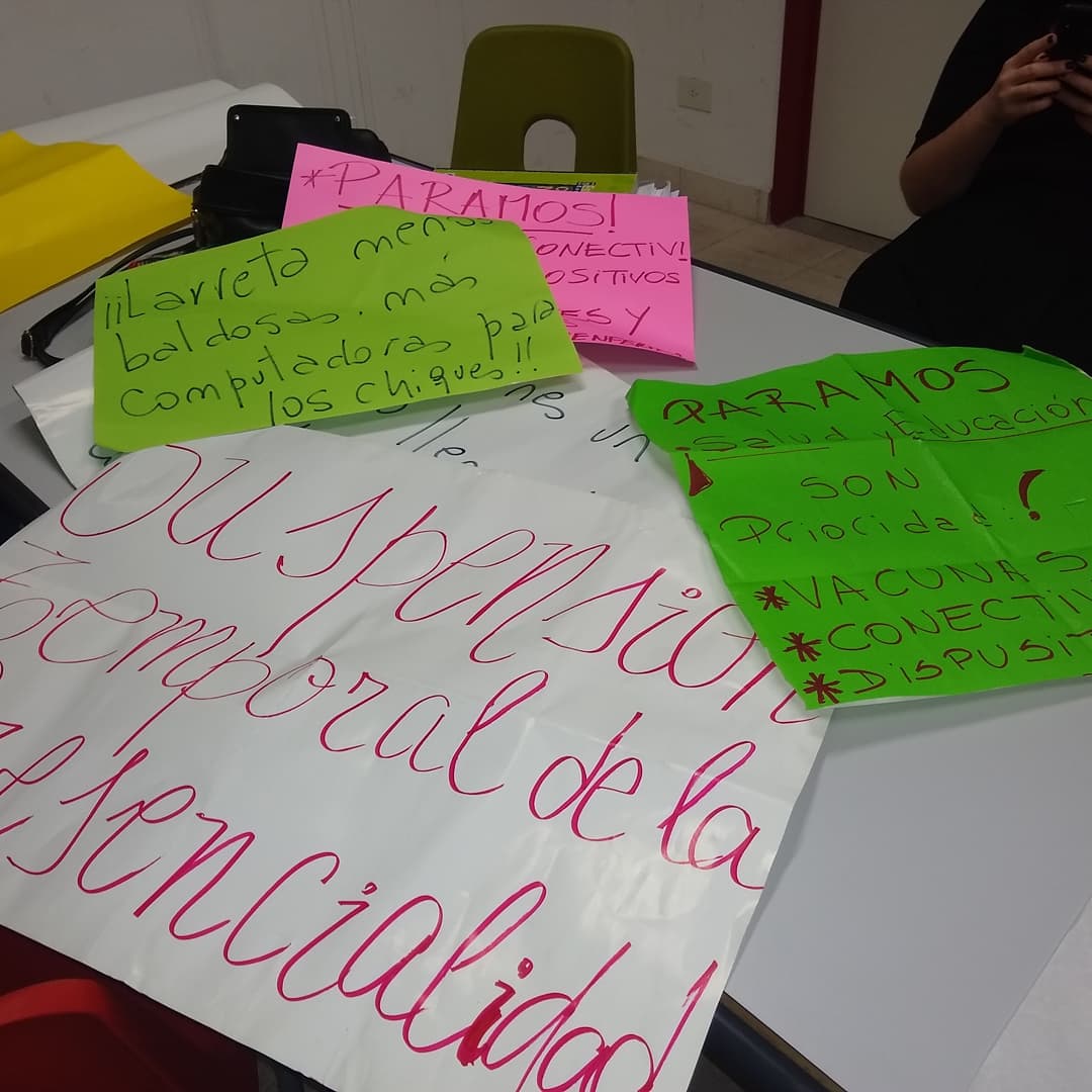 afiches sobre un escritorio que dice. suspensión temporal de la presencialidad. Menos baldosas mas computadoras para les chiques. Paramos salud y educación son prioridad.